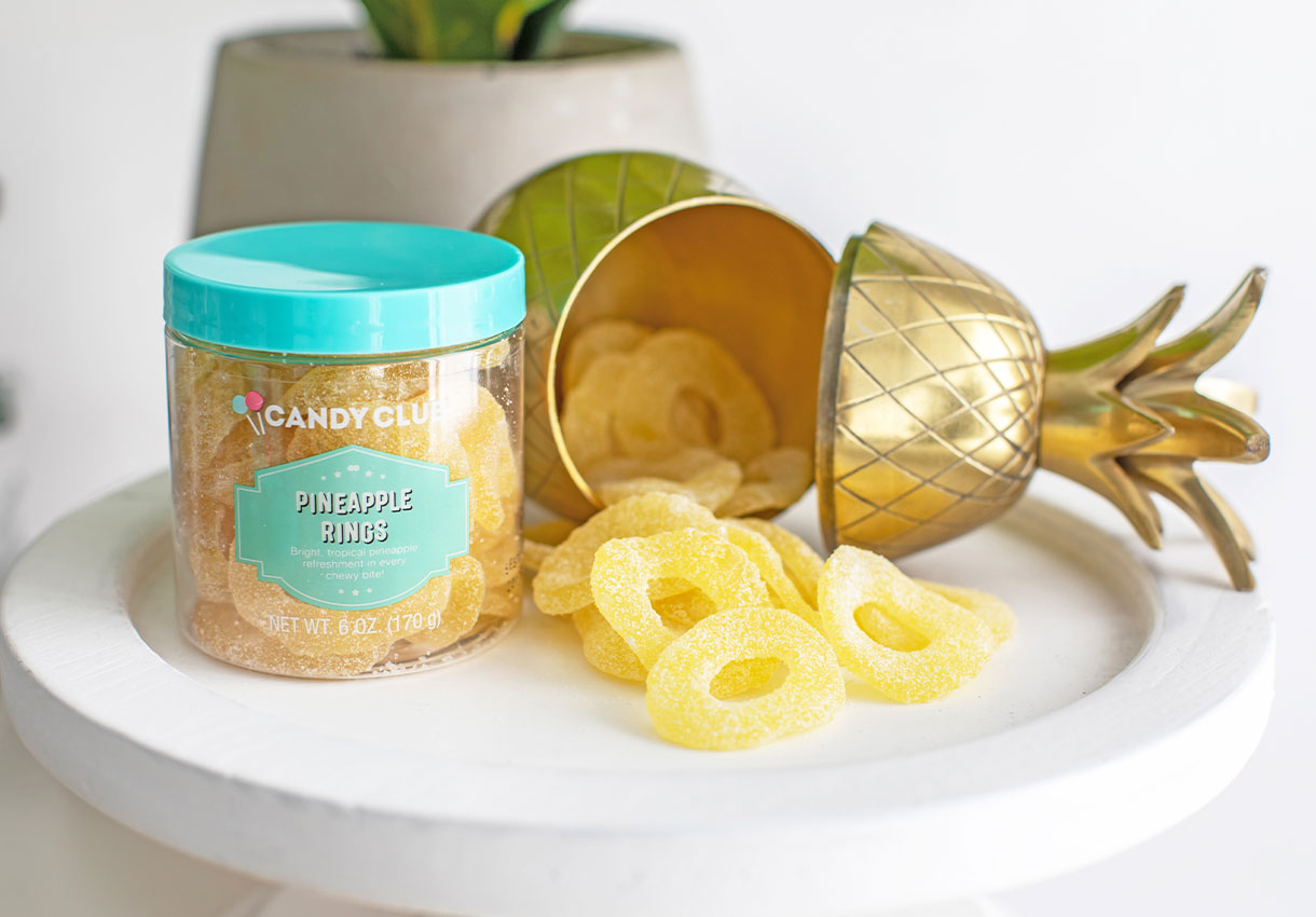 A cup of Candy Club's Pineapple Rings next to a gold pineapple display filled with pineapple rings