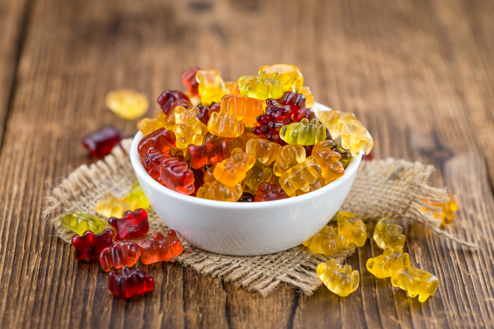 A bowl of autumn colored gummy bears on a wooden table. 